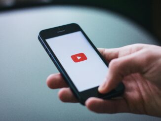 Close-up of a hand holding a smartphone displaying the YouTube app on the screen.