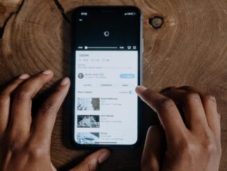 Overhead view of hands browsing videos on a smartphone placed on a wooden background.