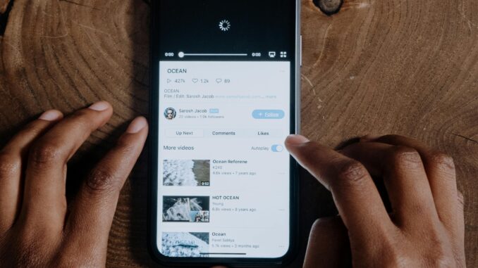 Overhead view of hands browsing videos on a smartphone placed on a wooden background.