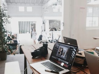 A bright, modern workspace featuring laptops, a camera, and a drawing tablet in an indoor office.