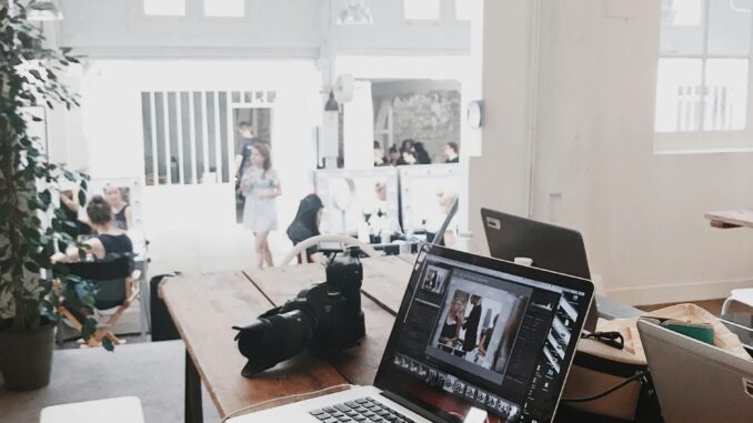 A bright, modern workspace featuring laptops, a camera, and a drawing tablet in an indoor office.