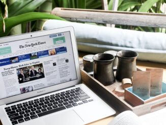 High angle of modern laptop with news on screen placed on table next to tin cups