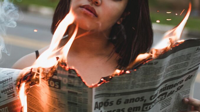 A woman stands outdoors holding a burning newspaper, capturing a dramatic and intense moment.