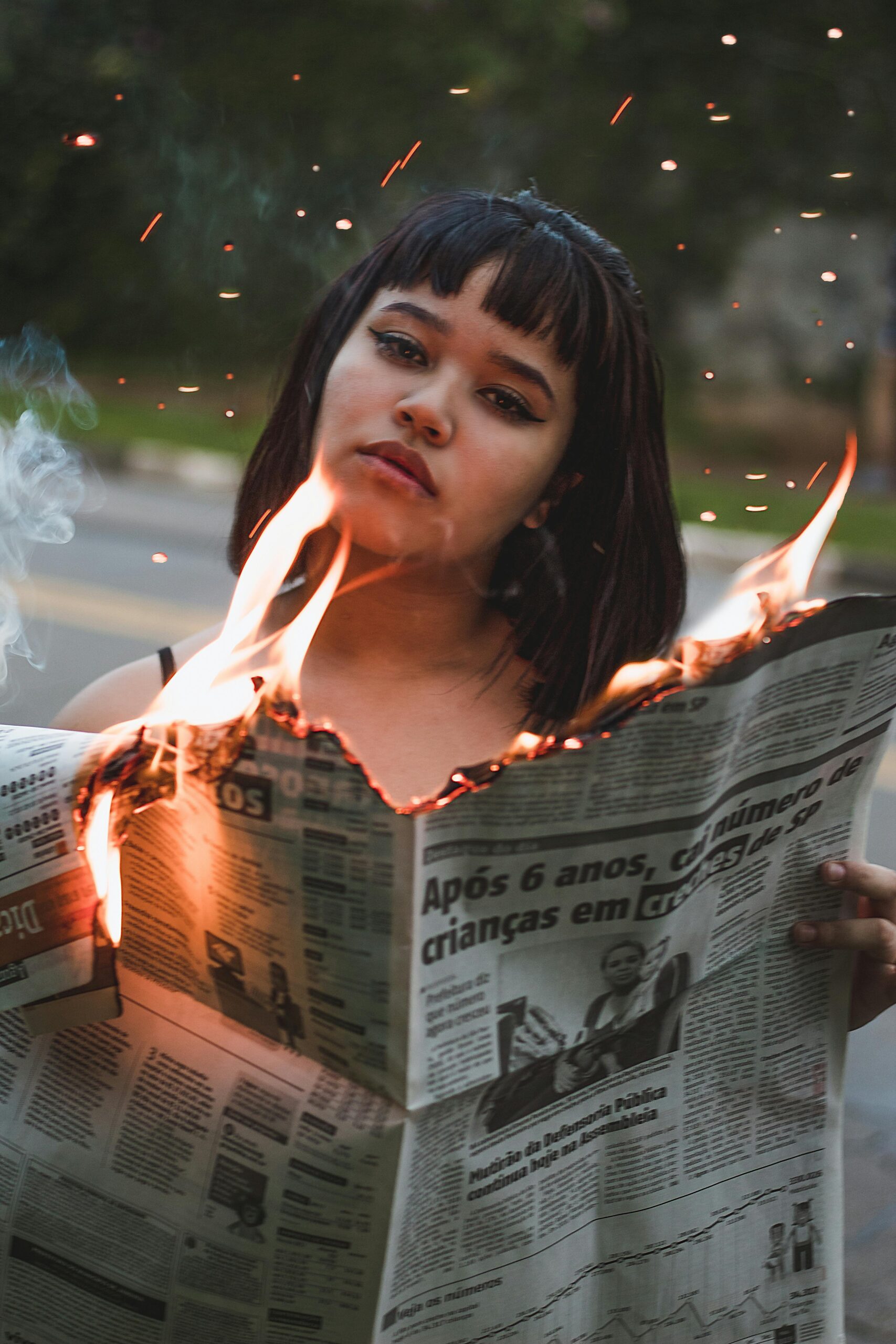 A woman stands outdoors holding a burning newspaper, capturing a dramatic and intense moment.