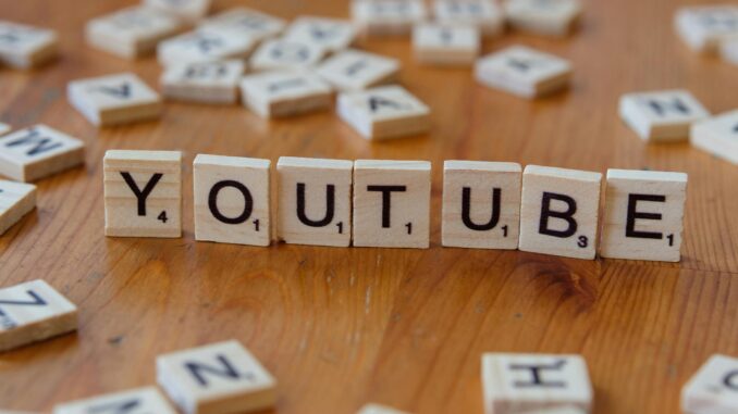 Wooden letter tiles spelling 'YOUTUBE' on a wooden surface, symbolizing video sharing and streaming.