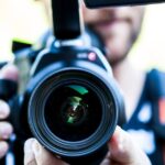 A close-up shot of a cameraman filming, focusing on the camera lens and equipment.