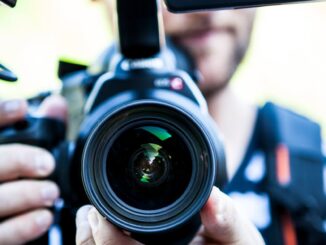A close-up shot of a cameraman filming, focusing on the camera lens and equipment.