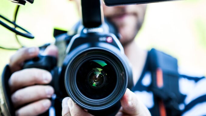 A close-up shot of a cameraman filming, focusing on the camera lens and equipment.