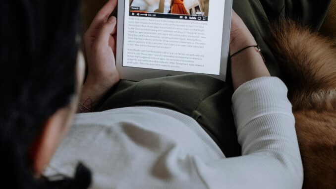 A woman reads an online article on a digital tablet while relaxing at home.