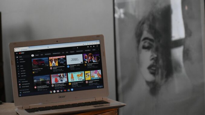 A cozy indoor setting with an Acer laptop displaying YouTube on a wooden table beside artwork.