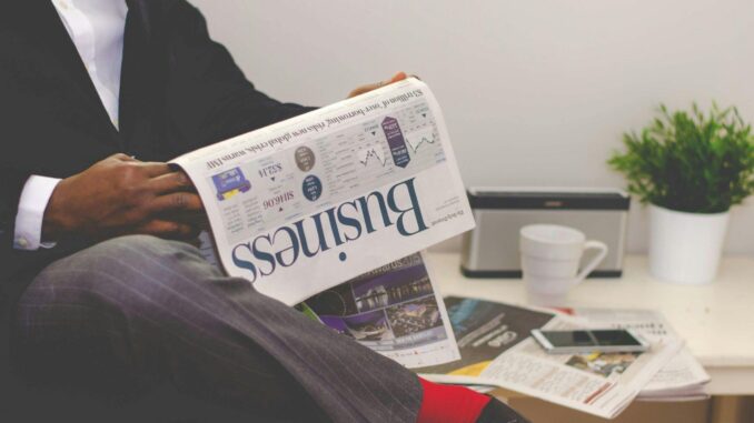 Businessman reading a financial newspaper at a desk, highlighting finance and commerce theme.