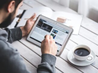 A man uses a tablet to browse news while enjoying a cup of coffee, stylus in hand.