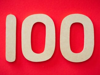 Close-up of numeral 100 in beige on a bright red background, emphasizing celebration.