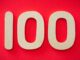 Close-up of numeral 100 in beige on a bright red background, emphasizing celebration.