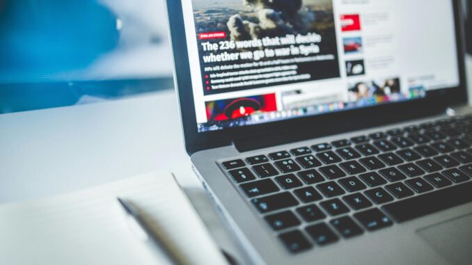 Open laptop displaying an online news article on a desk with a notebook nearby.