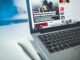 Open laptop displaying an online news article on a desk with a notebook nearby.