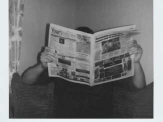 Person reading a newspaper at home in a vintage black and white style.