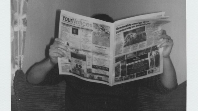 Person reading a newspaper at home in a vintage black and white style.