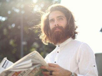 Young bearded man enjoying a sunny day while reading a newspaper outdoors.
