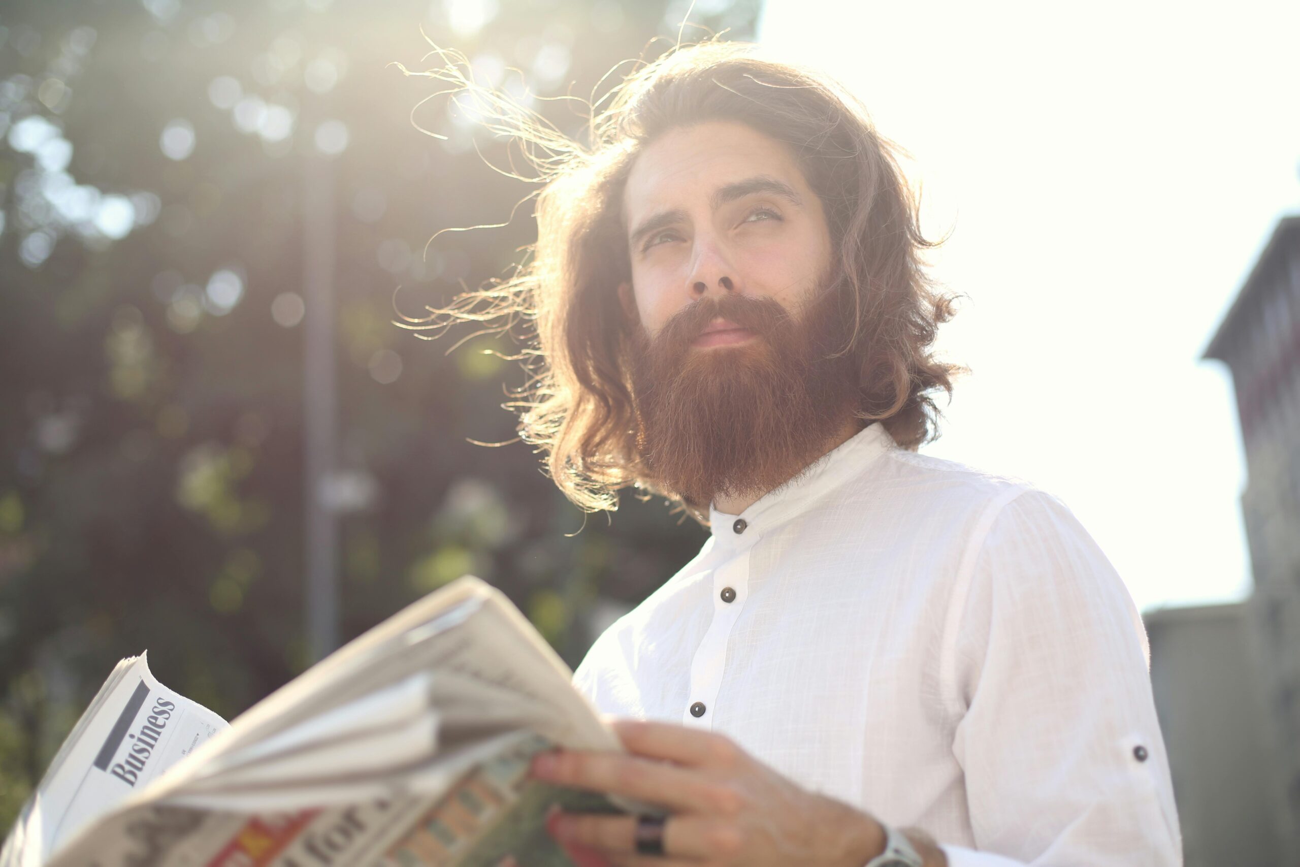 Young bearded man enjoying a sunny day while reading a newspaper outdoors.