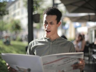 A young man is surprised while reading a newspaper at an outdoor cafe.