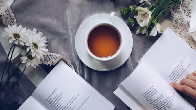 Inviting cozy reading setup with tea, poetry books, and fresh flowers on a table.