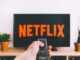 A hand holding a TV remote in front of a screen with Netflix, perfect for streaming and movie night themes.