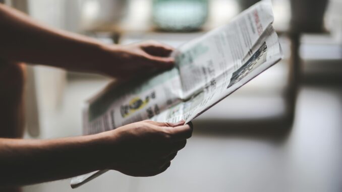 Hands holding a newspaper in a soft-lit, indoor environment, focusing on a relaxed reading moment.