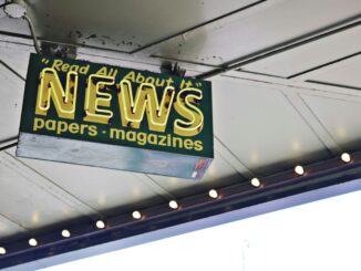 From below of illuminated signboard with news papers magazines inscriptions hanging on metal ceiling on street