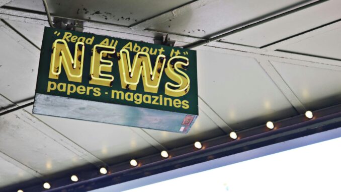 From below of illuminated signboard with news papers magazines inscriptions hanging on metal ceiling on street
