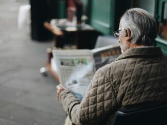 Elderly man reading a newspaper in an outdoor cafe setting, enjoying a peaceful moment.