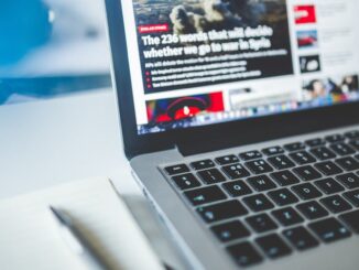 Open laptop displaying an online news article on a desk with a notebook nearby.