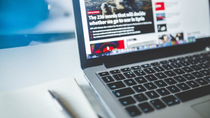 Open laptop displaying an online news article on a desk with a notebook nearby.