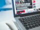 Open laptop displaying an online news article on a desk with a notebook nearby.