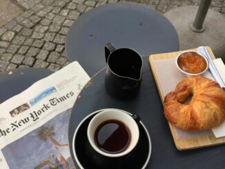 A cozy setup in Berlin featuring coffee, croissant, jam, and a newspaper on a cafe table.
