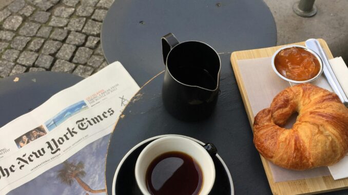 A cozy setup in Berlin featuring coffee, croissant, jam, and a newspaper on a cafe table.