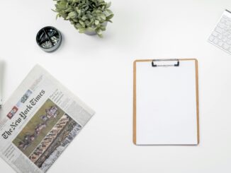 Clean flatlay of a home office desk with The New York Times, clipboard, and keyboard.