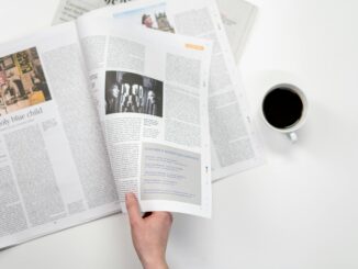 A close-up shot of a hand holding a newspaper with a coffee cup on a white surface.