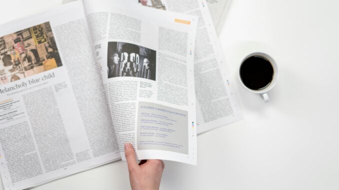 A close-up shot of a hand holding a newspaper with a coffee cup on a white surface.