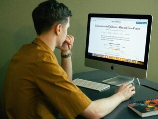 Man in a home office reading coronavirus map and case update on computer screen.