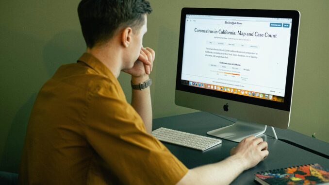 Man in a home office reading coronavirus map and case update on computer screen.