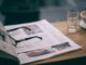 Eyewear on magazine with text in columns and illustrations near cup with saucer on wooden table in cafeteria
