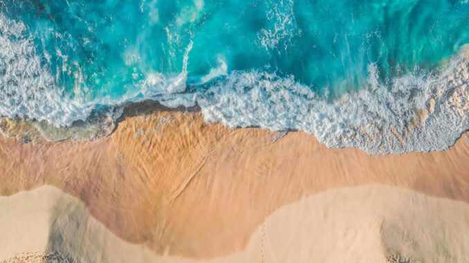 Stunning aerial view of turquoise waves hitting a sandy beach, perfect for nature lovers.