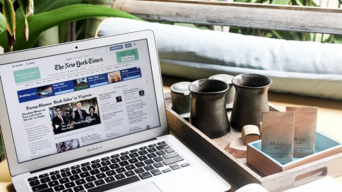High angle of modern laptop with news on screen placed on table next to tin cups