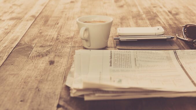 A warm vintage morning setup with coffee, newspaper, and smartphone on wooden table.