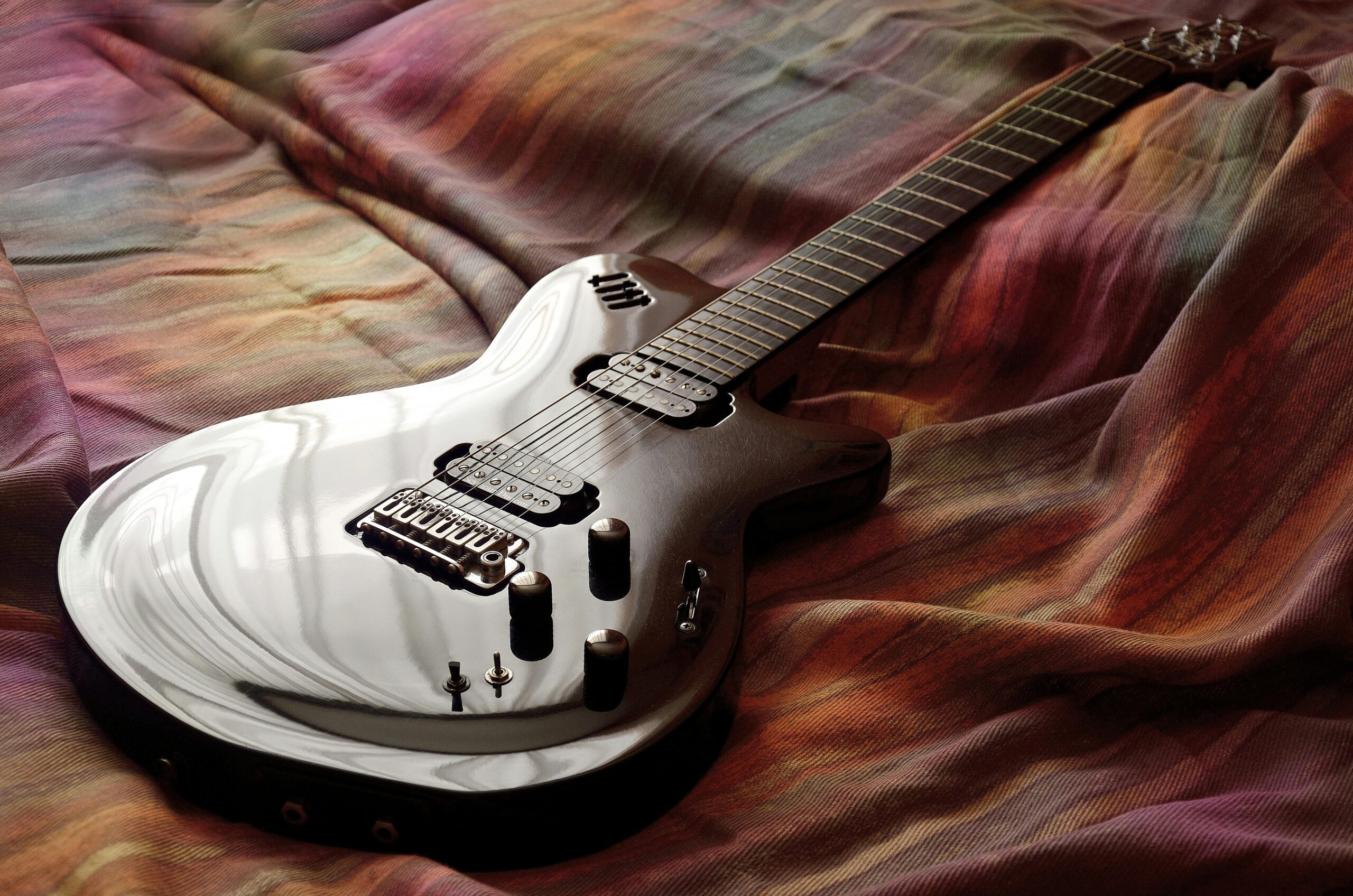Sleek electric guitar resting on colorful fabric, captured with artistic lighting.