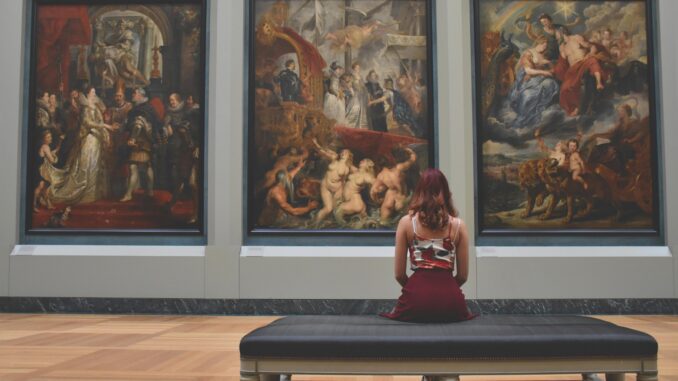 A woman observes classic paintings in an elegant museum gallery.