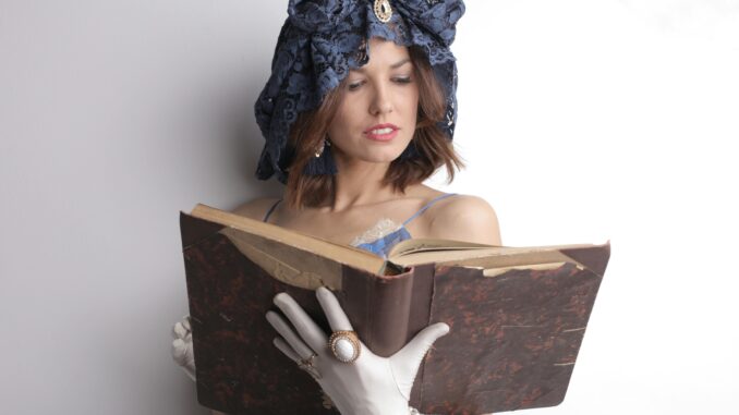 A woman wearing a vintage hat and gloves reads an old book indoors.