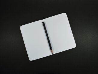 Top view of an open blank notebook with a pencil on a black background, perfect for creative projects.