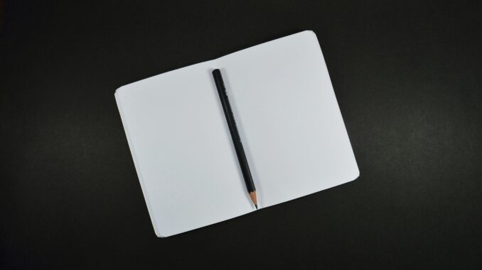 Top view of an open blank notebook with a pencil on a black background, perfect for creative projects.